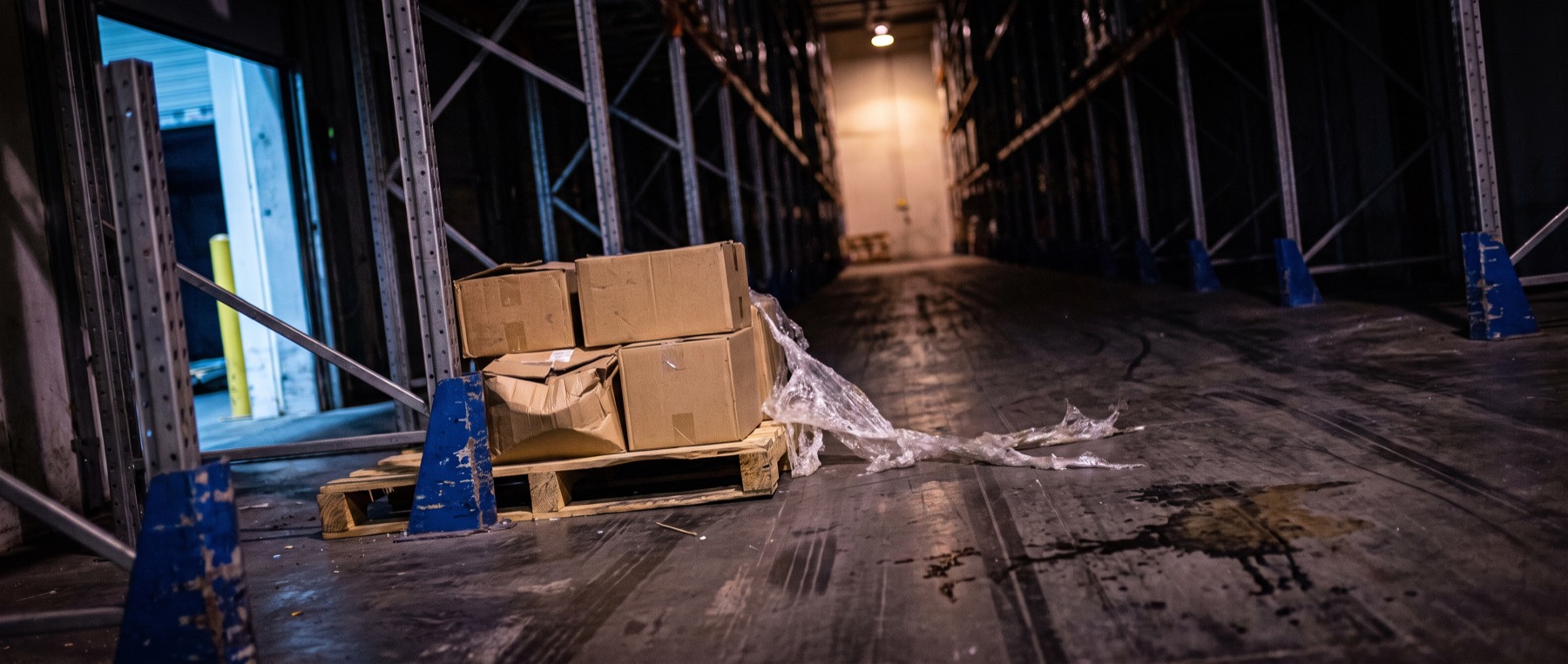 A part-loaded pallet standing alone in a dark warehouse aisle, shrink wrap trailing onto the floor.